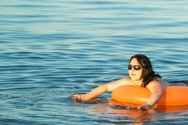 A brunette woman with glasses swims in the sea on a swimming circle. — Stockfoto