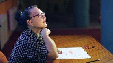 Gözlüklü sanatçı, beyaz kağıt üzerinde pastel teknikte çalışır.