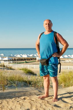 Denizin arka planına karşı sahilde şortlu bir adam ve tişörtlü bir adam..