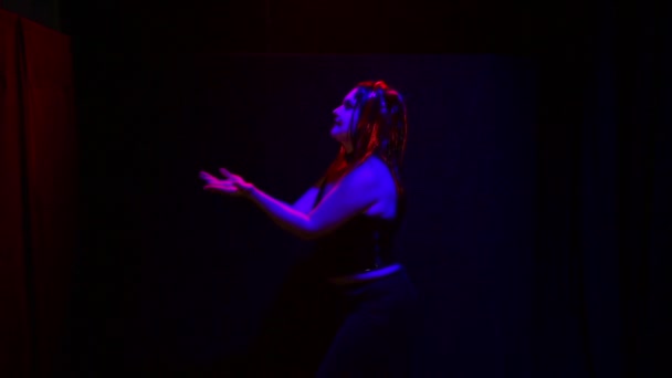En kvinna i form av en djävul med ett olycksbådande leende dansar i rött ljus på en svart bakgrund. — Stockvideo
