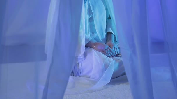 Uma jovem muçulmana de branco faz uma oração atrás de uma cortina branca — Vídeo de Stock