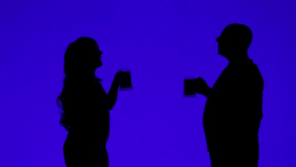 Silhueta de uma mulher e um homem bebendo cerveja de canecas em um fundo azul — Vídeo de Stock