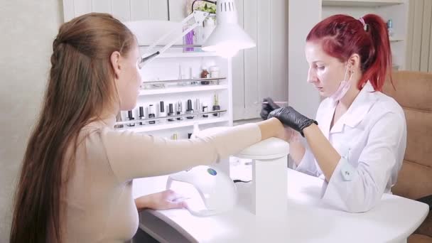 Manicurist kvinna i kosmetiska bad är att tillämpa gel på klienter naglar. Flickan torkar naglarna i en ultraviolett lampa — Stockvideo