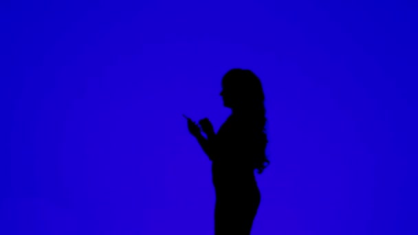 Mavi arka planda cep telefonuyla konuşan kıvırcık saçlı bir kadının silueti. — Stok video
