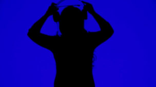 Силуэт женщины в наушниках и танцующей под музыку на синем фоне — стоковое видео