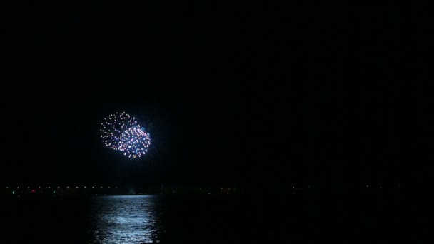 Sparks of festive fireworks in the night sky above the river reflecting in the water — ストック動画