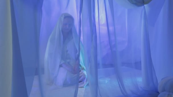 A young Muslim woman in white makes a prayer behind a white curtain — Stockvideo