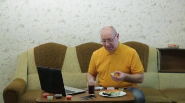 Masada dizüstü bilgisayarı olan gözlüklü bir adam rulo yer ve çalışır.