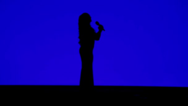 Silhouette di una snella cantante sul palco con un microfono su sfondo blu . — Video Stock