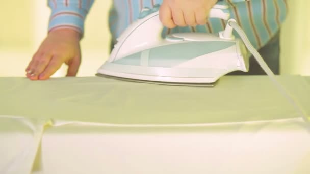 Mujer ama de casa planchando ropa de colores en una tabla de planchar en casa. El plan medio — Vídeo de stock