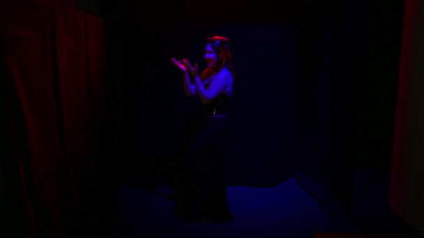 Devil woman with an ominous smile dancing in red lighting on a black background. — Wideo stockowe