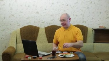 Masada dizüstü bilgisayarı olan gözlüklü bir adam rulo yer ve çalışır.