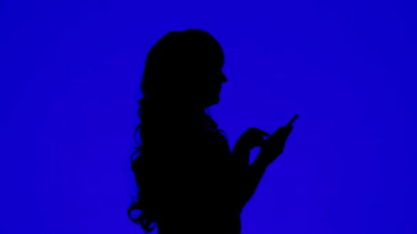 Silueta de una mujer hablando en un teléfono celular sobre un fondo azul — Vídeos de Stock