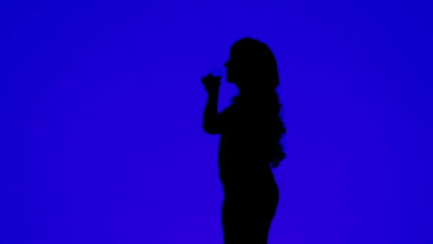 Silhouette di una donna con capelli ricci che beve vino da un bicchiere su uno sfondo blu . — Video Stock