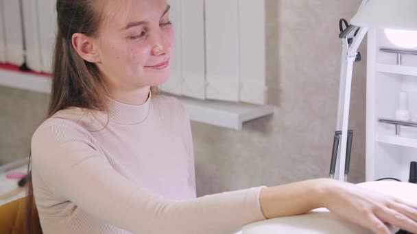 Kvinna manikyrist i en skönhetssalong applicerar violett gellack på naglarna på en kund. Flickan torkar naglarna i en speciell lampa. — Stockvideo