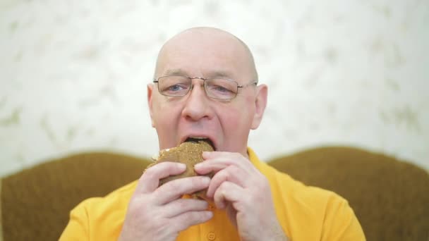 Un homme souriant mange un hamburger synsys juteux — Video