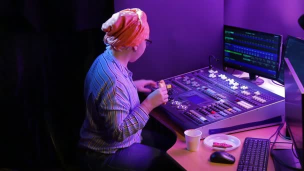 Een joodse vrouw in een hoofddoek, een lichtontwerper, programmeert het licht voor een show en eet fastfood — Stockvideo