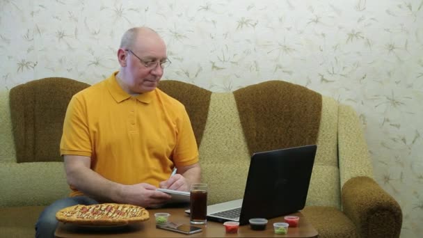 Человек за столом с ноутбуком заканчивает работу перед ужином пиццы — стоковое видео