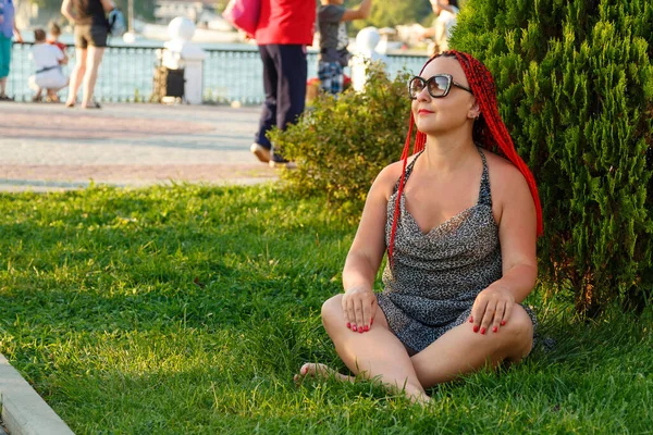 Hermosa mujer con el pelo rojo está sentado en la hierba en el parque . — Foto de Stock