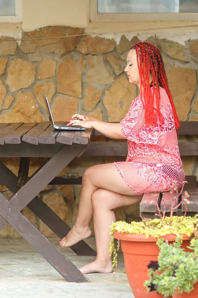 한 젊은 여성이 휴가 중 베란다에서 노트북으로 원격으로 작업합니다.. — 스톡 사진