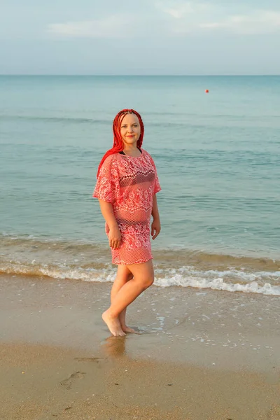 Mujer joven con el pelo rojo en la orilla del mar en una túnica de encaje . — Foto de Stock