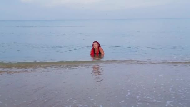 一位身穿黑色泳衣、头戴红色辫子的犹太妇女坐在海里，从汹涌的浪涛中摔了下来. — 图库视频影像