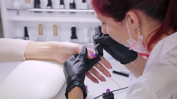 Femme manucure dans un salon de beauté applique un vernis gel violet sur les ongles d'un client — Video