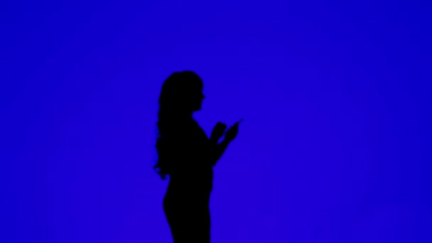 Silhouette of a woman with curly hair talking on a cell phone on a blue background — Stockvideo