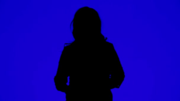 Kulaklık takan ve mavi arka planda müzik eşliğinde dans eden bir kadının silueti. — Stok video