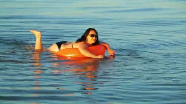 Uma mulher morena de maiô e óculos nada em um círculo de natação no mar perto da costa — Vídeo de Stock