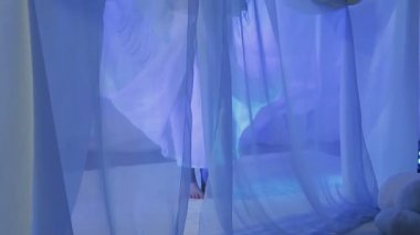 A young bride is dancing on the eve of the wedding behind a white curtain