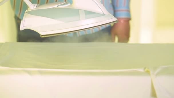Strijkijzer in een vrouwelijke hand gladstrijkt wit linnen op een strijkplank — Stockvideo