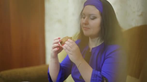 Femme souriante mangeant un hamburger tiré à travers le rideau — Video