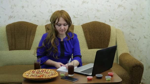 Женщина за столом с ноутбуком заканчивает работу перед ужином пиццы — стоковое видео
