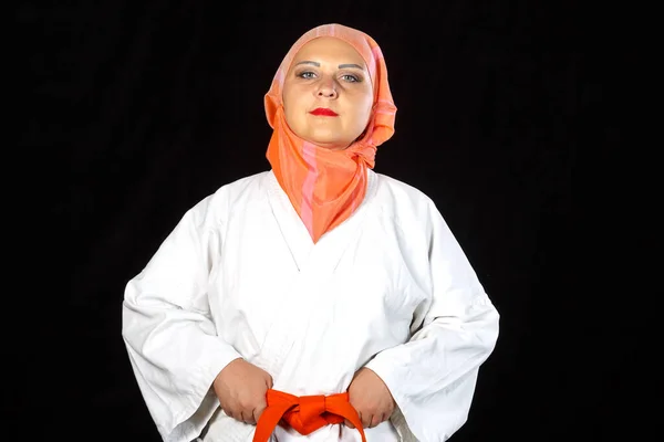 Junge muslimische Frau in Kimono und Schal beim Karatetraining vor schwarzem Hintergrund. Nahaufnahme. — Stockfoto