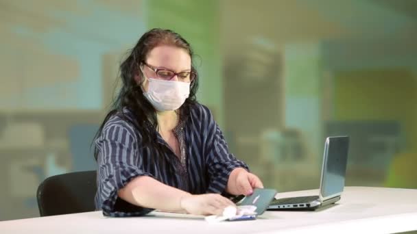 Женщина в кабинете в медицинской маске дезинфицирует технику, чтобы предотвратить коронавирус — стоковое видео