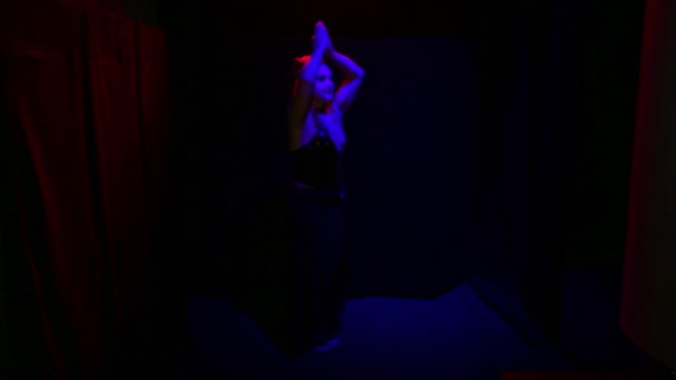 Een vrouw in de vorm van een duivel met een onheilspellende glimlach danst in rood licht op een zwarte achtergrond — Stockvideo