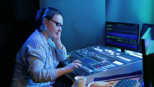 A young woman with glasses, a lighting designer, programs the light for a show and drinks coffee — Stock Video