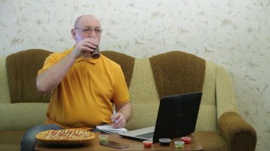 A man at a table with a laptop is finishing work before a pizza dinner