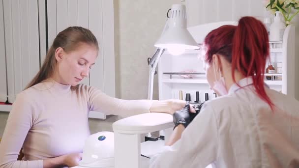 La mujer manicurista en baño cosmético está aplicando gel en las uñas de los clientes. La chica se seca las uñas en una lámpara ultravioleta — Vídeo de stock