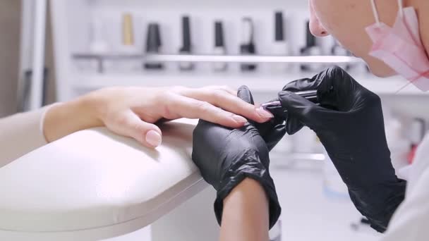 Mujer manicurista en un salón de belleza aplica gel en las uñas de un cliente . — Vídeo de stock