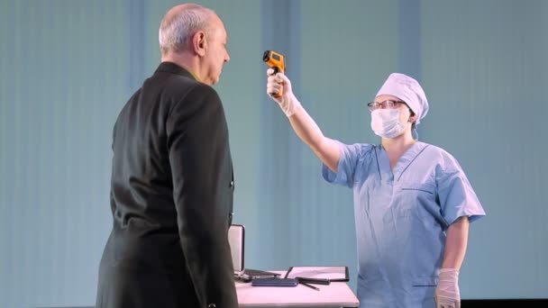 Женщина-врач в медицинской маске измеряет температуру мужчины удаленно до начала рабочего дня — стоковое видео