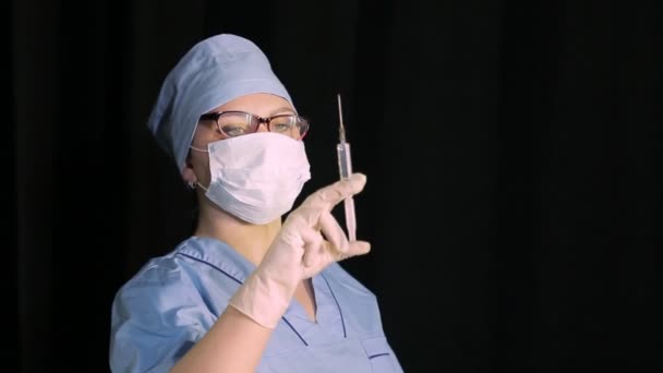 Vrouwelijke arts in een medisch masker met een spuit in de hand op een zwarte achtergrond — Stockvideo