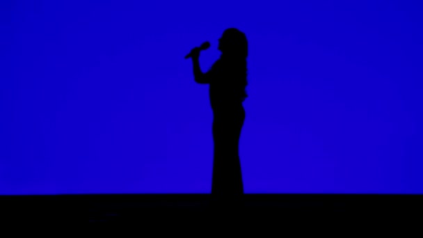 Silhouette d'une chanteuse élancée sur scène avec un microphone sur fond bleu — Video