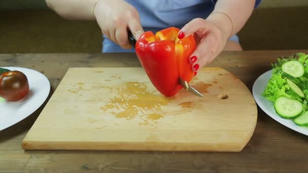 Kvinnen skjærer rød pepper på et trebrett til salat. – stockvideo