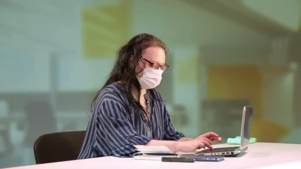 De vrouw op kantoor typt op een computer met een medisch masker. — Stockvideo