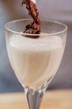 Bir kadın eli muzlu, dondurmalı ve çikolatalı smoothie serpiyor..