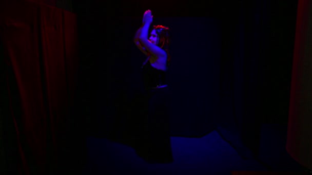 Дьяволица со зловещей улыбкой танцует в красном свете на черном фоне — стоковое видео