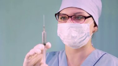 Elinde şırıngayla tıbbi maskeli bir kadın doktor.