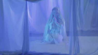 Beyazlı genç bir kadın beyaz perdenin arkasında dua ediyor.